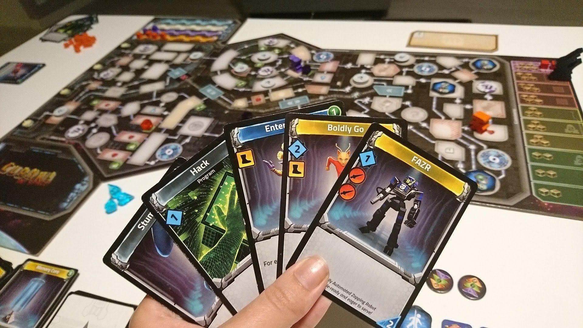 Kädessä Clank in Spacen kortteja, taustalla pelilauta