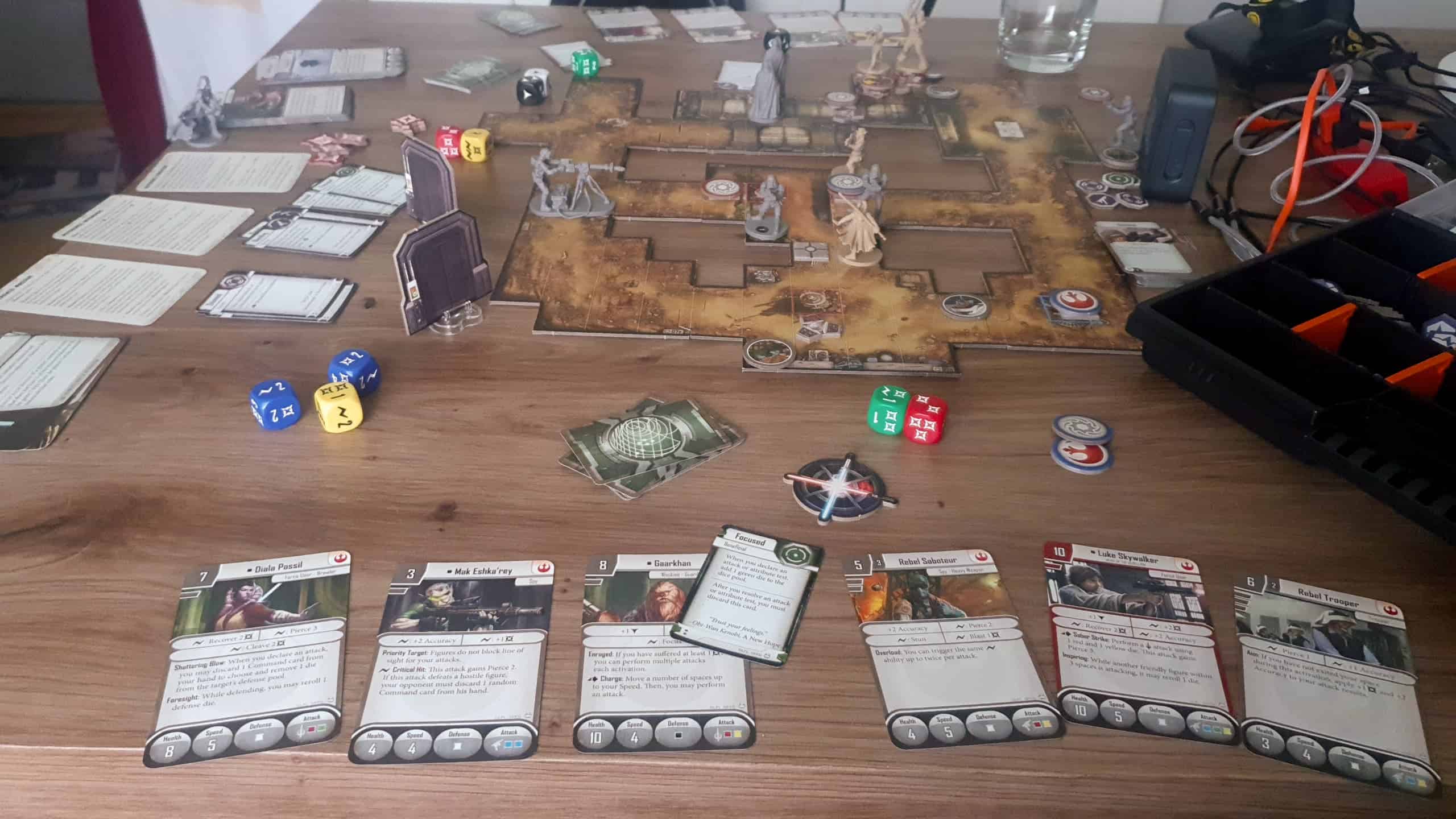 Imperial Assault -peli käynnissä. Pelilautaa on rakenneltu palasista, taistelukenttänä on pienehkö käytäväverkosto. Laudalla on neljä kapinallista, vastassaan viisi imperiumin yksikköä. Etualalla on kapinallisten kortteja.