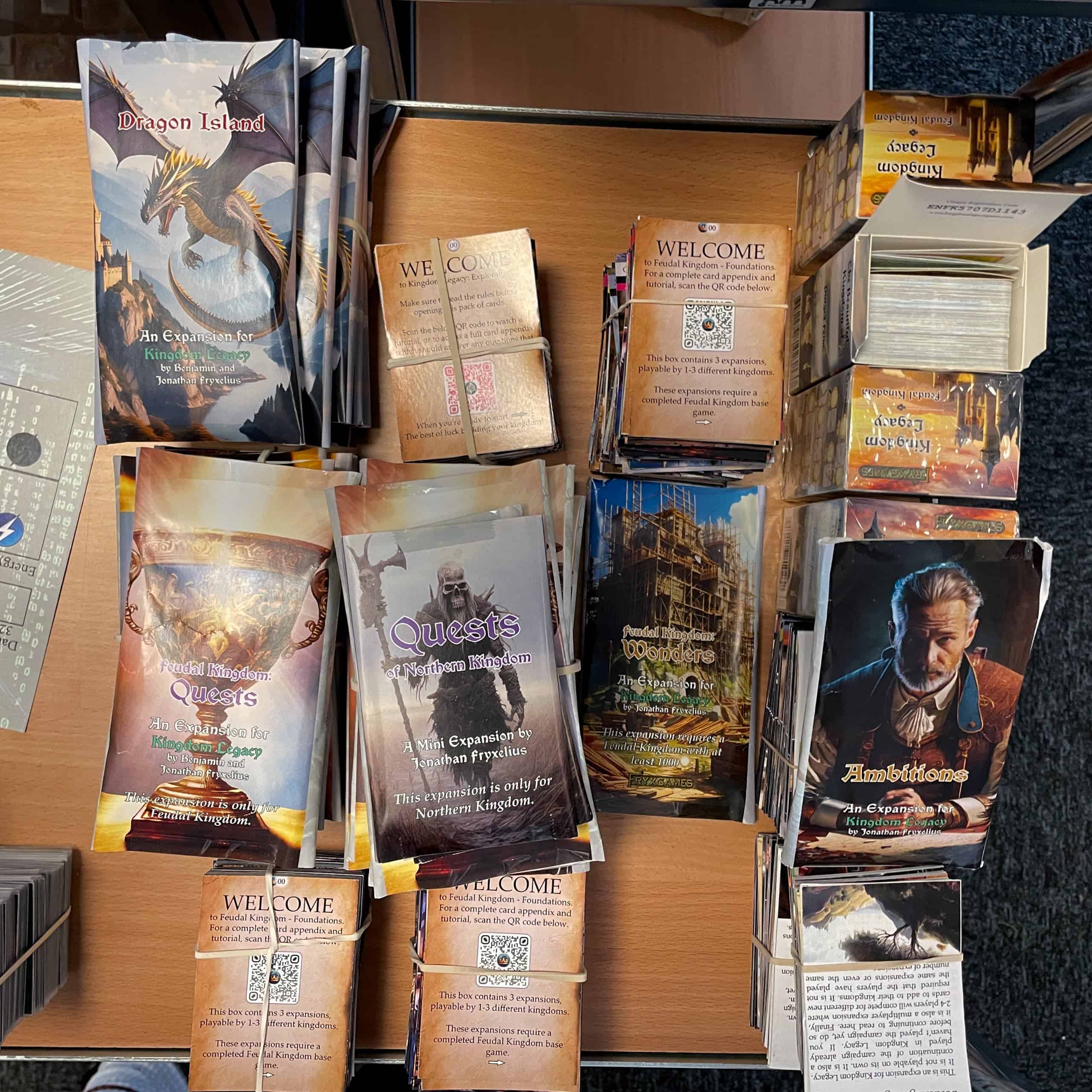 Monta pinoa Kingdom Legacy -pelin korttipakkoja ja lisäosia pöydällä.