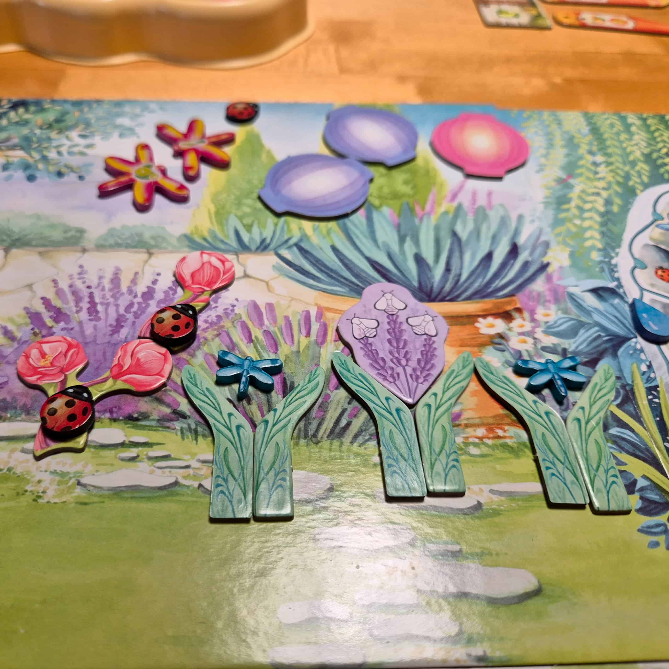 Lähikuva Pergolan puutarhalaudalta, jossa on magnolioita leppäkerttuineen, laventelia sudenkorennoin ja kukkivana, isoja sudenkorentoja ja muutama lyhty.
