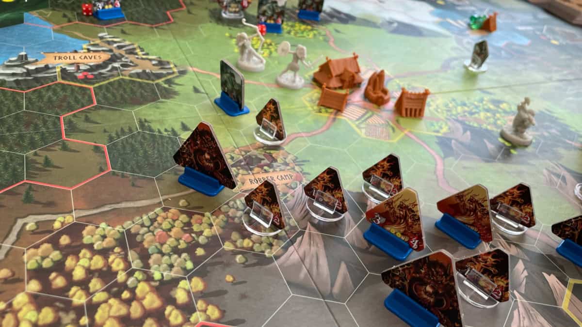 Fate: Defenders of Grimheim -laudalla on heksaruutuihin jaettua maisemaa. Taustalla näkyy kylän ruskeat muovirakennukset ja etualalla niitä lähestyvä Fire Horde -hirviölauma, 11 kolmion muotoista pahvilätkää niitä pystyssä pitävissä telineissä. Laudalla on myös muita hirviöitä ja pelaajien valkoisia figuureja.