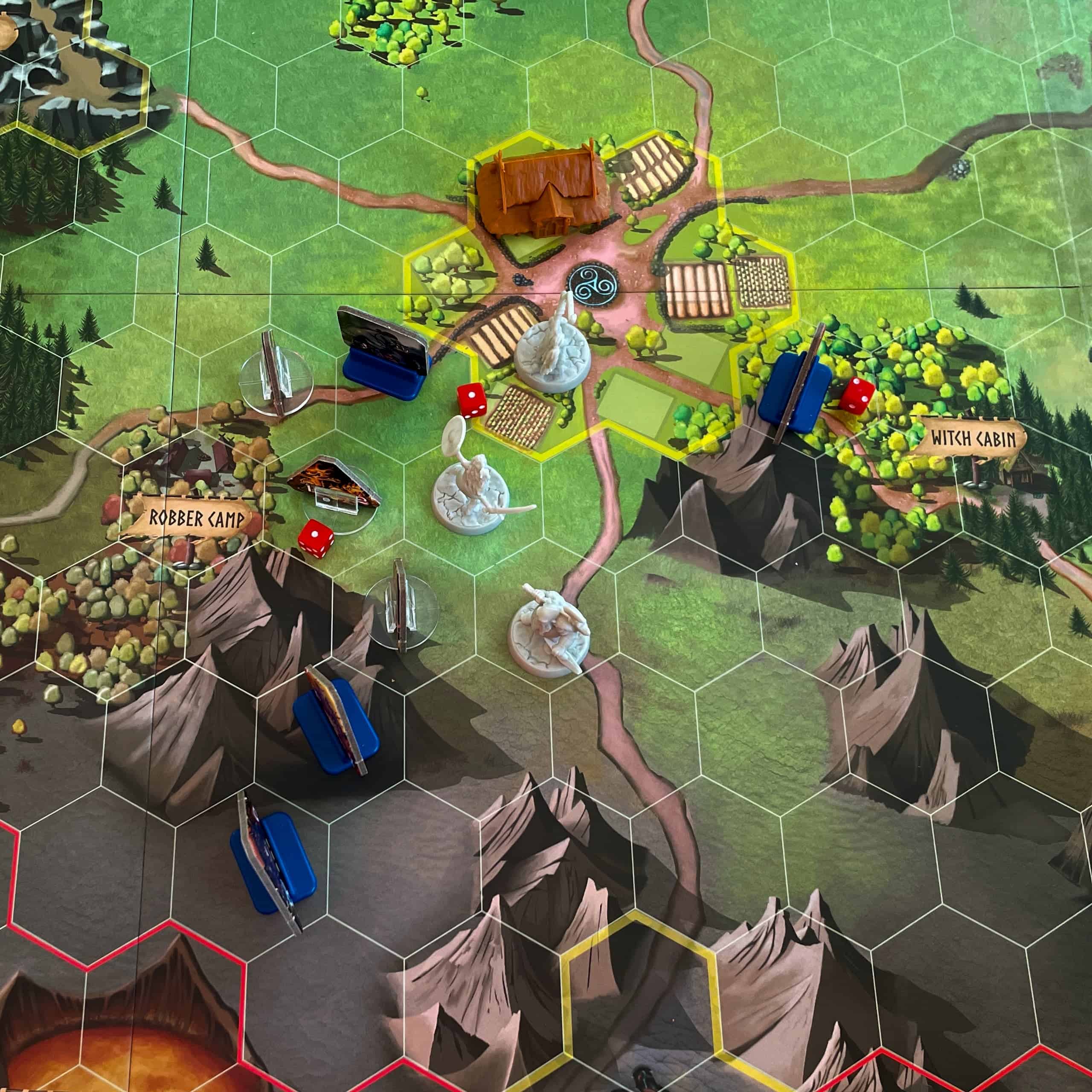 Lähikuva pelilaudan keskellä olevasta kylästä, jossa on jäljellä enää yksi rakennus. Sankarit puolustavat yhä kylää lähestyviä vihollisia vastaan. Kylän lähistöllä näkyy noidan mökki ja rosvojen leiri. Tulivuoren suunnasta on lähestymässä Fire Horde -hirviöitä.