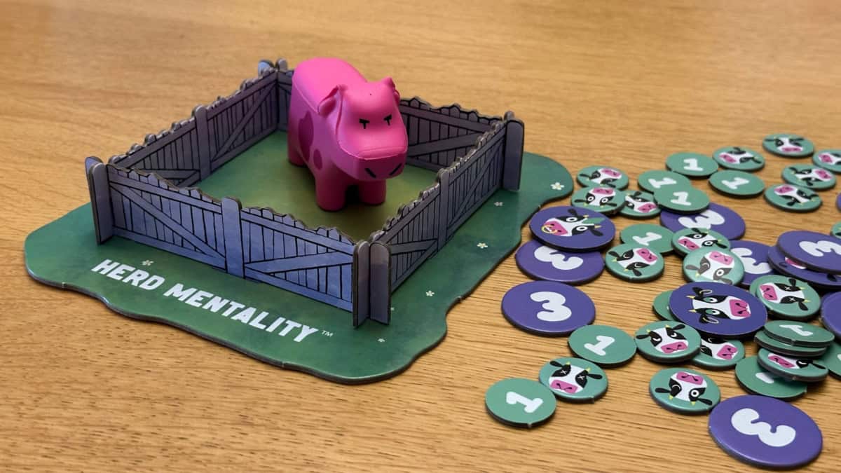 Pahvinen lehmäaitaus, jossa on pinkki kumilehmä ja vieressä turkooseja ja violetteja pahvisia pistelätkiä.