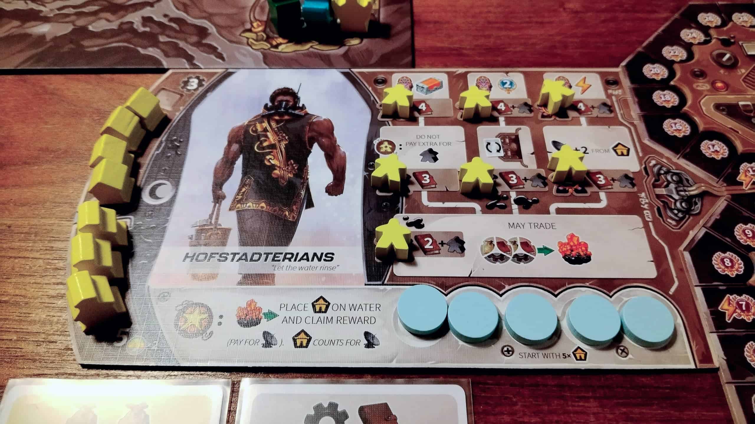 Hofstadterianien heimolauta. Laudassa on kuva lihaksikkaasta vedenkantajasta, meeplejä ja mökkejä ja erikoiskykyjä.