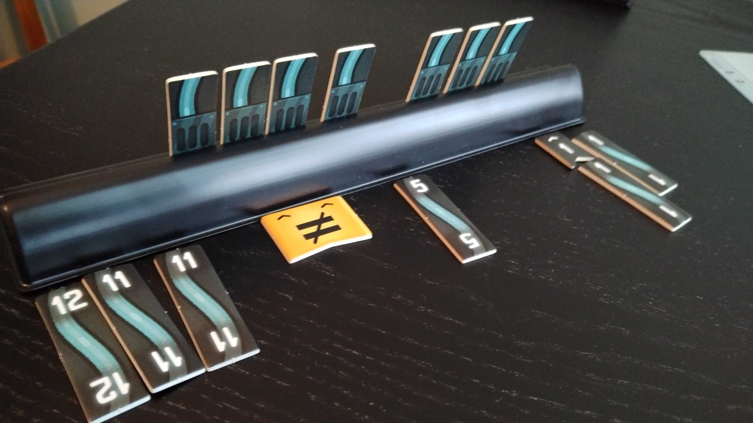 Pelaajan laattateline, jossa on johdot 12, 11 ja 11, välissä neljä piilossa olevaa johtoa joiden kohdalla keltainen epäyhtäläisyysmerkkilaatta, sitten viitonen, kolme johtoa ja kaksi ykköstä.