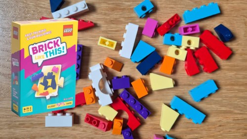 Brick Like This! -pelin laatikko ja taustalla värikkäitä pieniä Lego-palikoita levällään pöydällä.