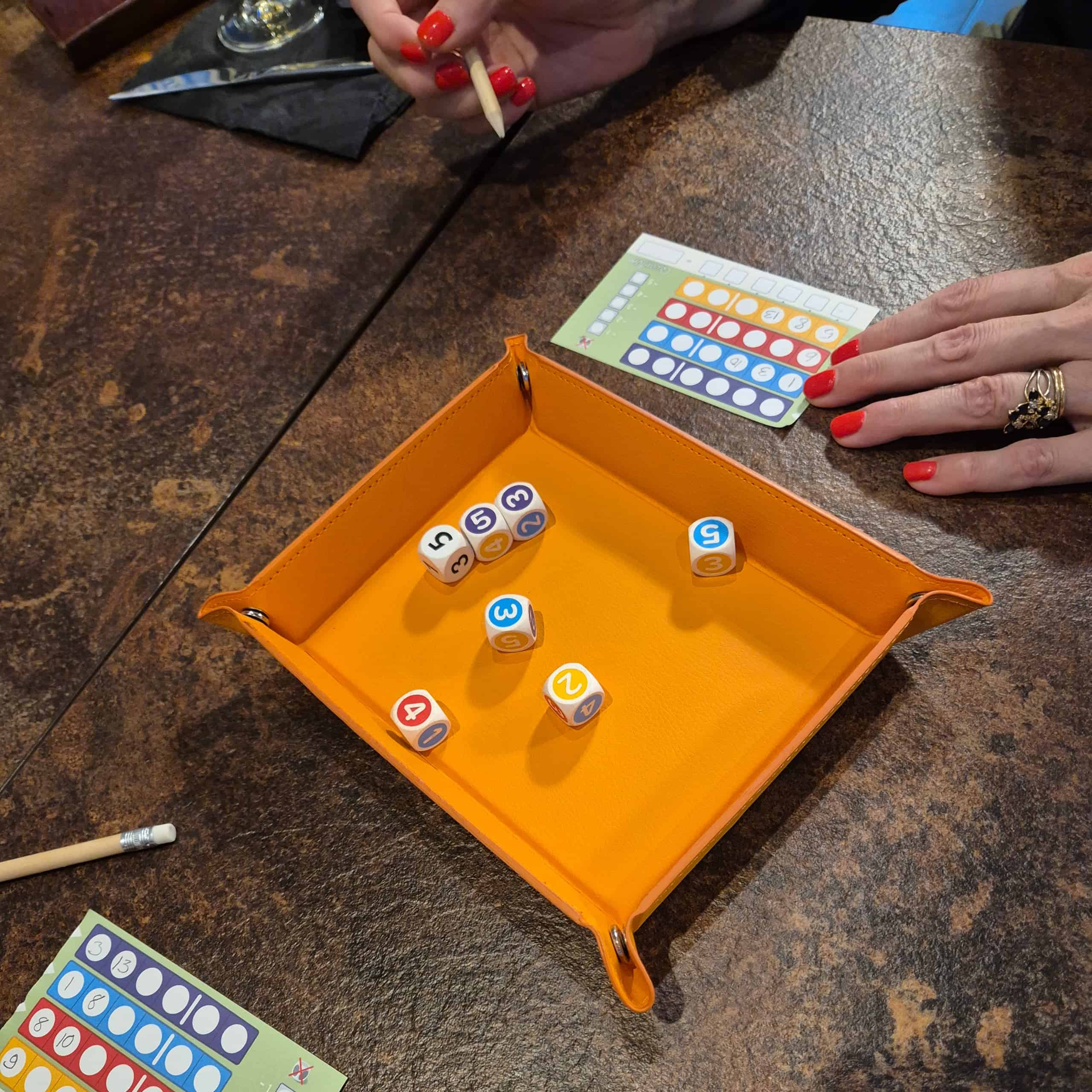 Qwantumin pelaamista ravintolapöydässä, keskellä pöytää on oranssi noppavati ja siinä seitsemän eri värejä ja numeroita yhdistelevää noppaa.