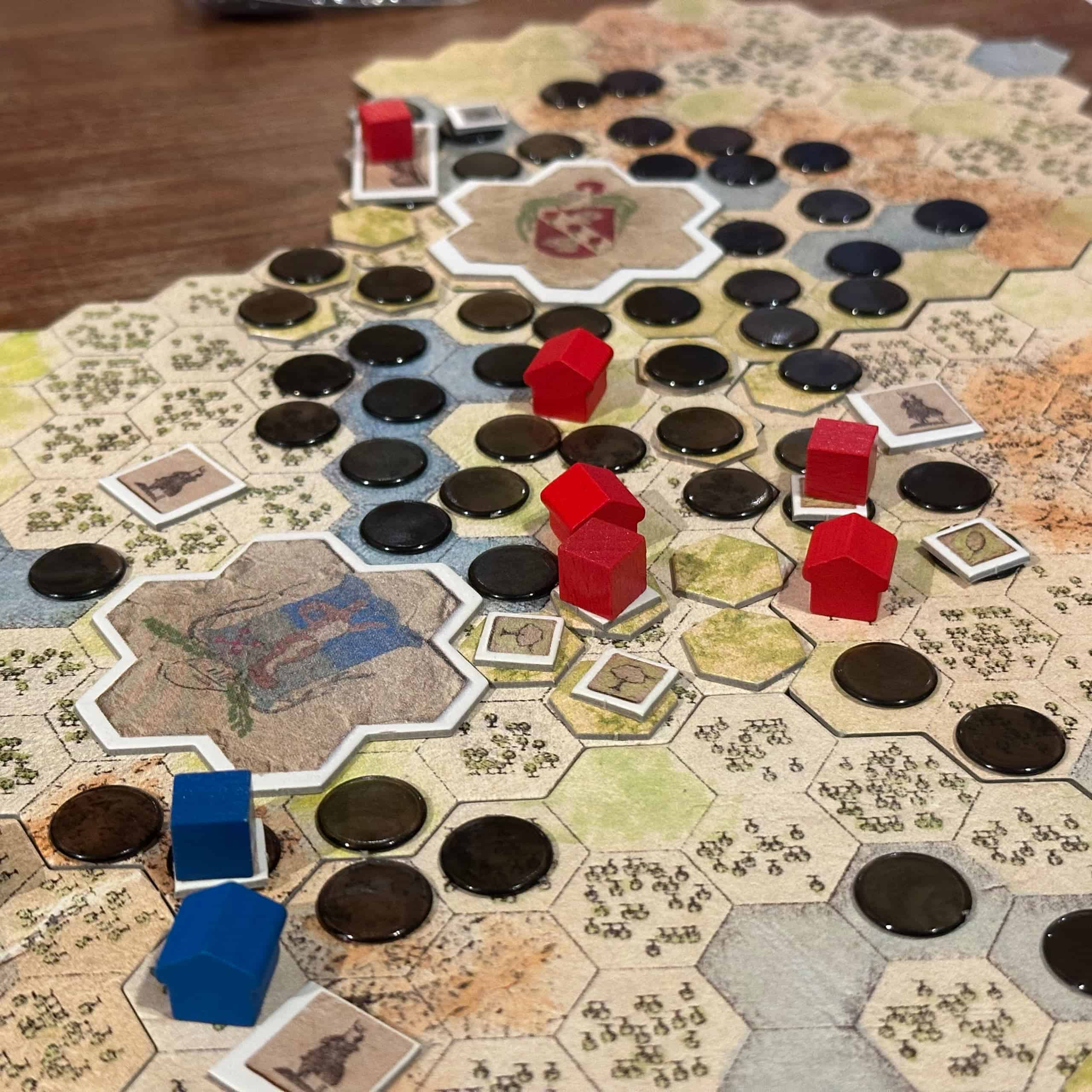 Lähikuva Antiquityn pelilaudasta, joka on mustien saastelätkien peittämä. Laudalla on myös sinisen ja punaisen pelaajan kaupungit, maatiloja ja majataloja.