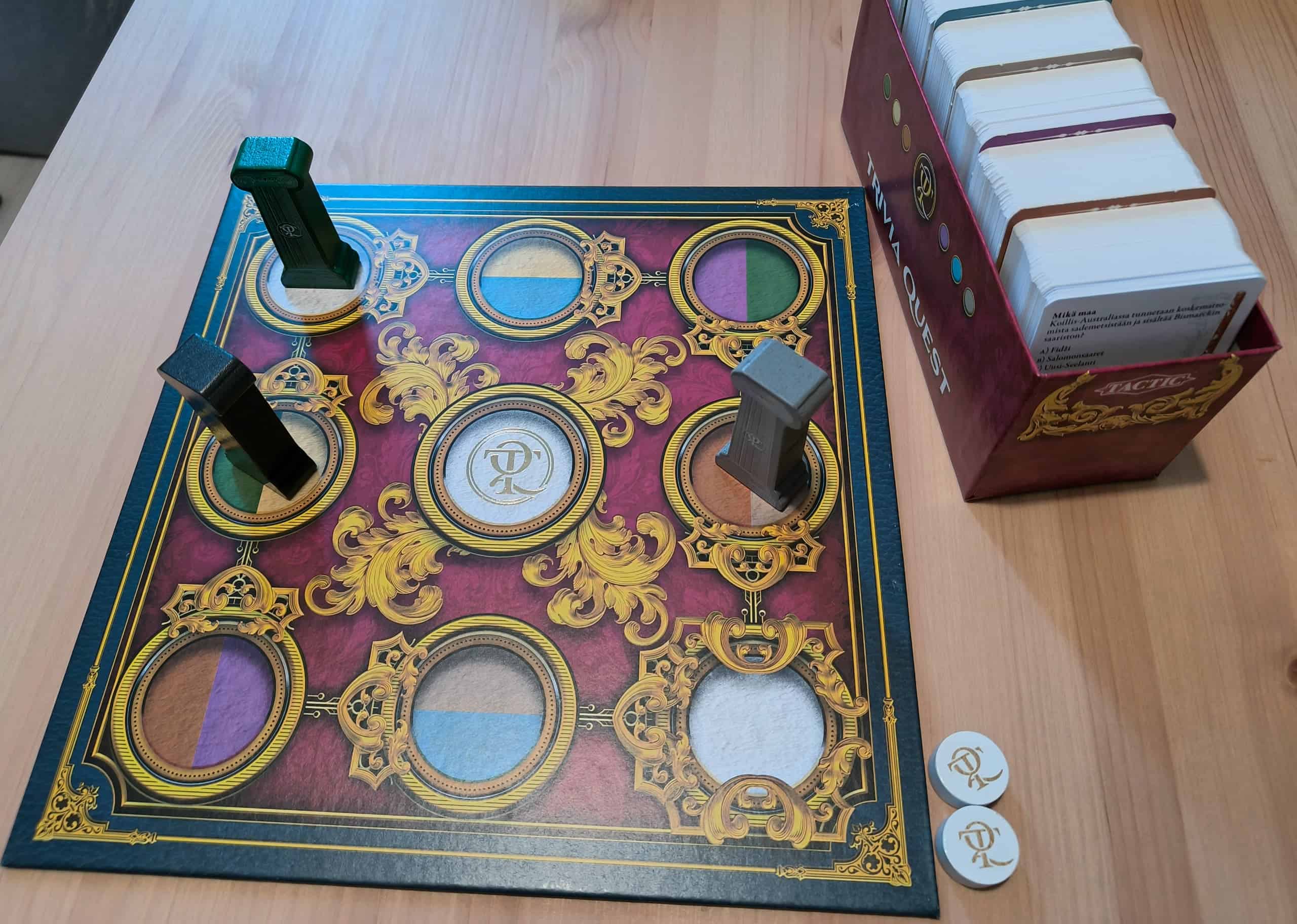 Trivia Questin pelilaudalla on yhdeksän ympyrää 3×3-muodostelmassa. Nappulat ovat puisia pilareita. Laudan vieressä on laatikollinen kysymyskortteja.