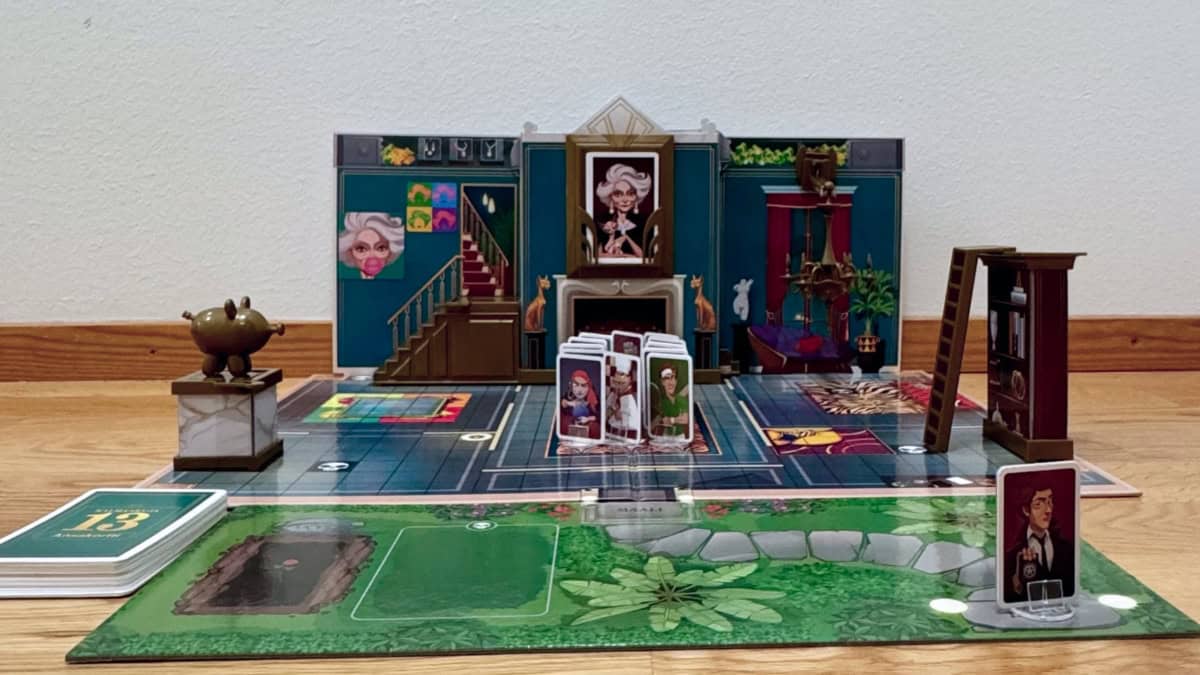 Kalmankuja 13:n pelilauta levitettynä lattialle seinän viereen. Pelihahmot ovat valmiina pöydän äärellä, etsivä on saapumassa ja ansat on viritetty.