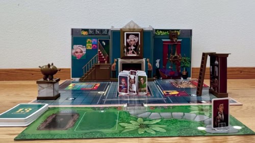 Kalmankuja 13:n pelilauta levitettynä lattialle seinän viereen. Pelihahmot ovat valmiina pöydän äärellä, etsivä on saapumassa ja ansat on viritetty.