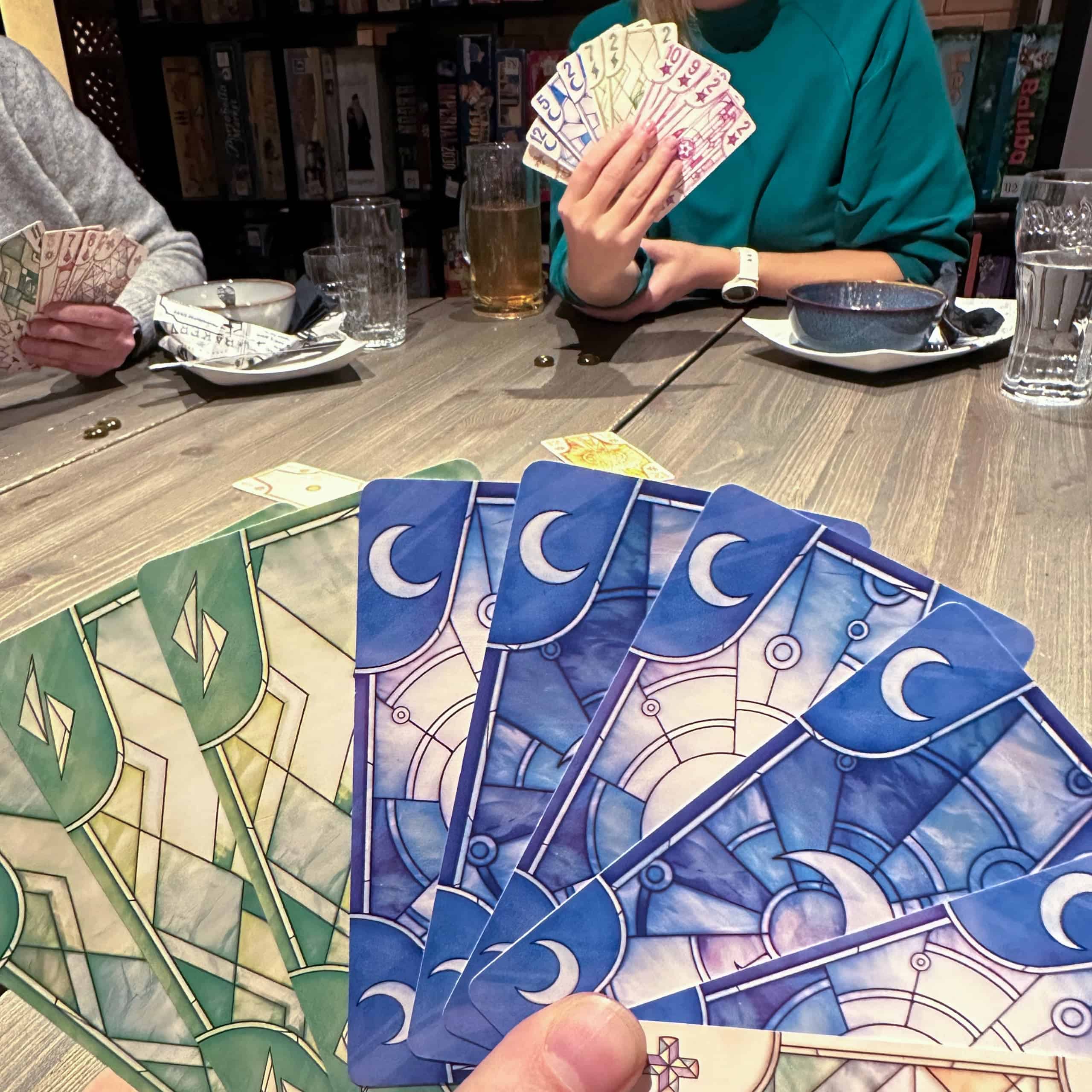 Luzin kortteja. Etualalla pelaajan oma käsi, josta näkyy vain korttien väri. Taustalla muita pelaajia, joiden korttien numerot näkyvät.