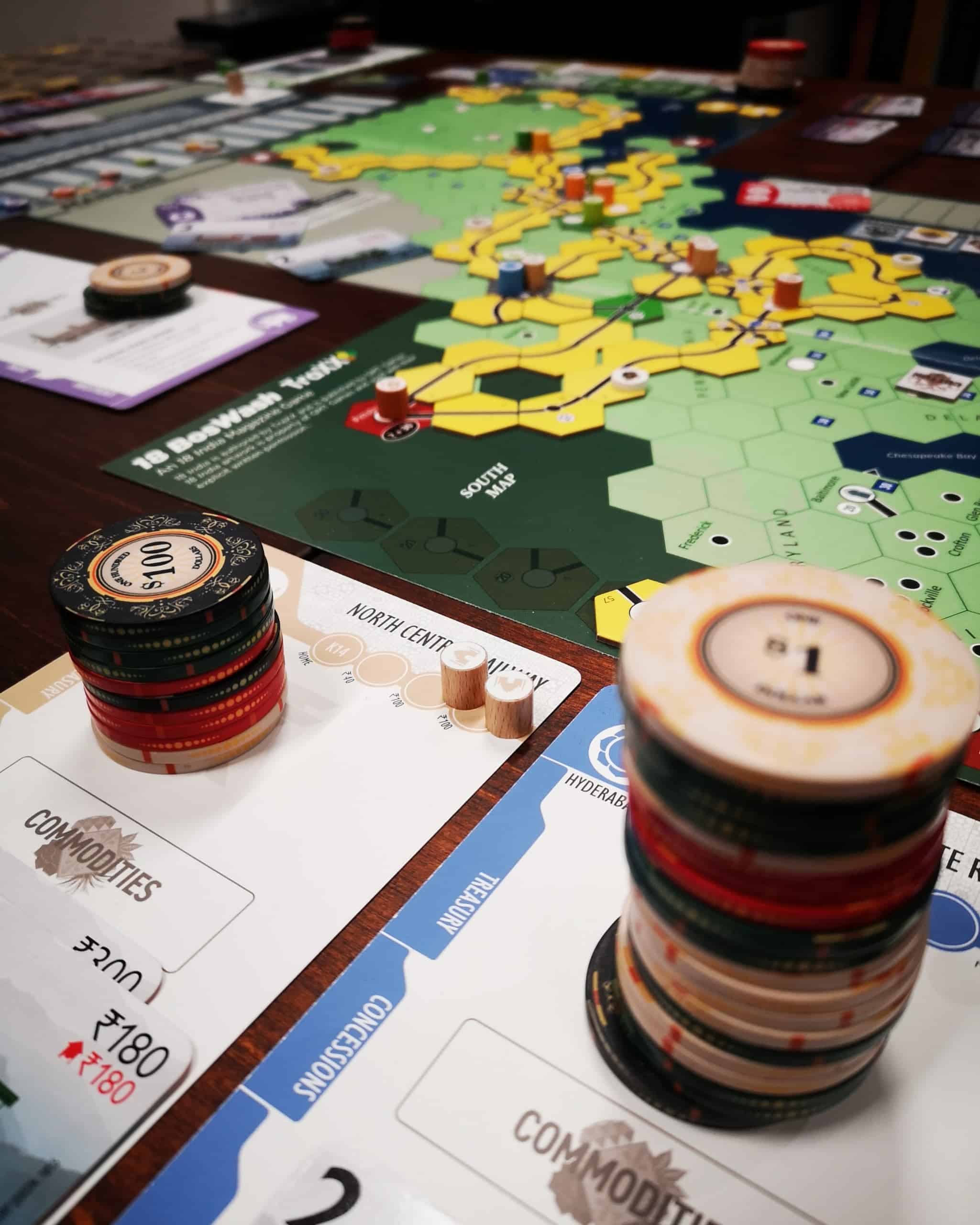 Etualalla kahden rautatien charterit, joiden päällä korkeat pinkat pokerichippejä. Taustalla 18 BosWashin pelilauta, johon on rakennettu runsaasti keltaista rataa.