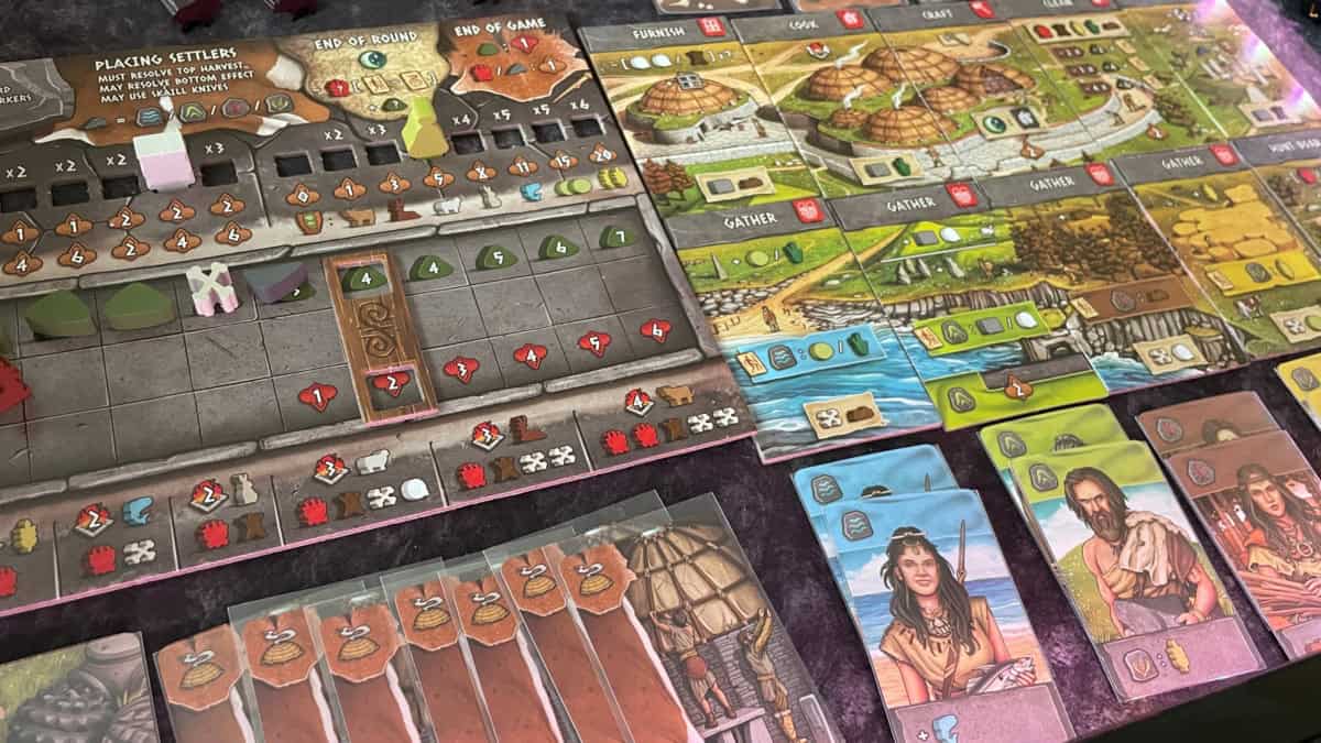 Lähikuva Skara Braen pelilaudasta, jossa on paljon erilaisia ratoja ja symboleita. Laudan vieressä on toimintolaattoja, ja niiden alla ihmisiä kuvaavia kortteja.
