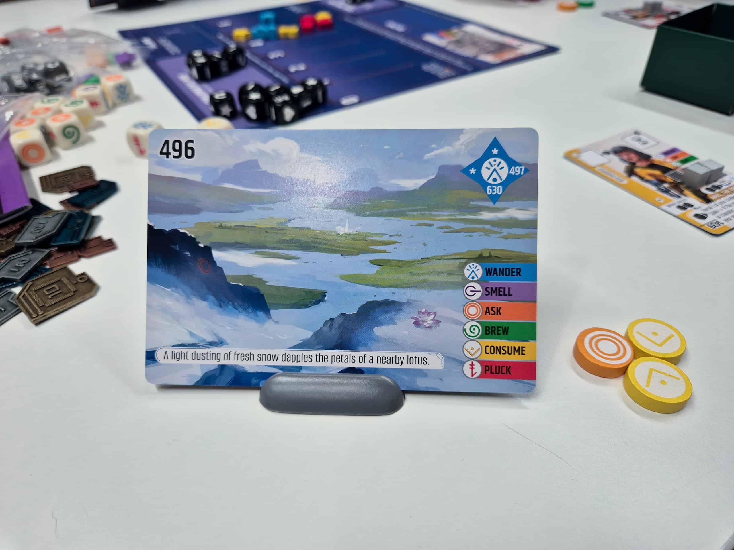 Vantagen maisemakortti pystyssä telineessään. Kortti kuvaa lumista näkymää vuorenrinteeltä alas veden täyttämään laaksoon. Kortissa lukee "A light dusting of fresh snow dapples the petals of a nearby lotus" ja toimintoina on tarjolla "Wander", "Smell", "Ask", "Brew", "Consume" ja "Pluck".