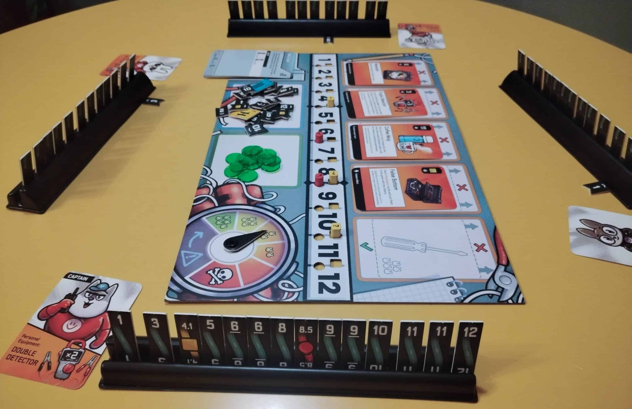 Keskellä on pelilauta ja ympärillä neljän pelaajan laattatelineet. Vasemmalla on merkitty johto 3, toisella puolella lautaa ehkä 6 ja oikealla 1. Etualalla olevalla pelaajalla on kapteenikortti, jolla voi tehdä tupla-arvauksen.