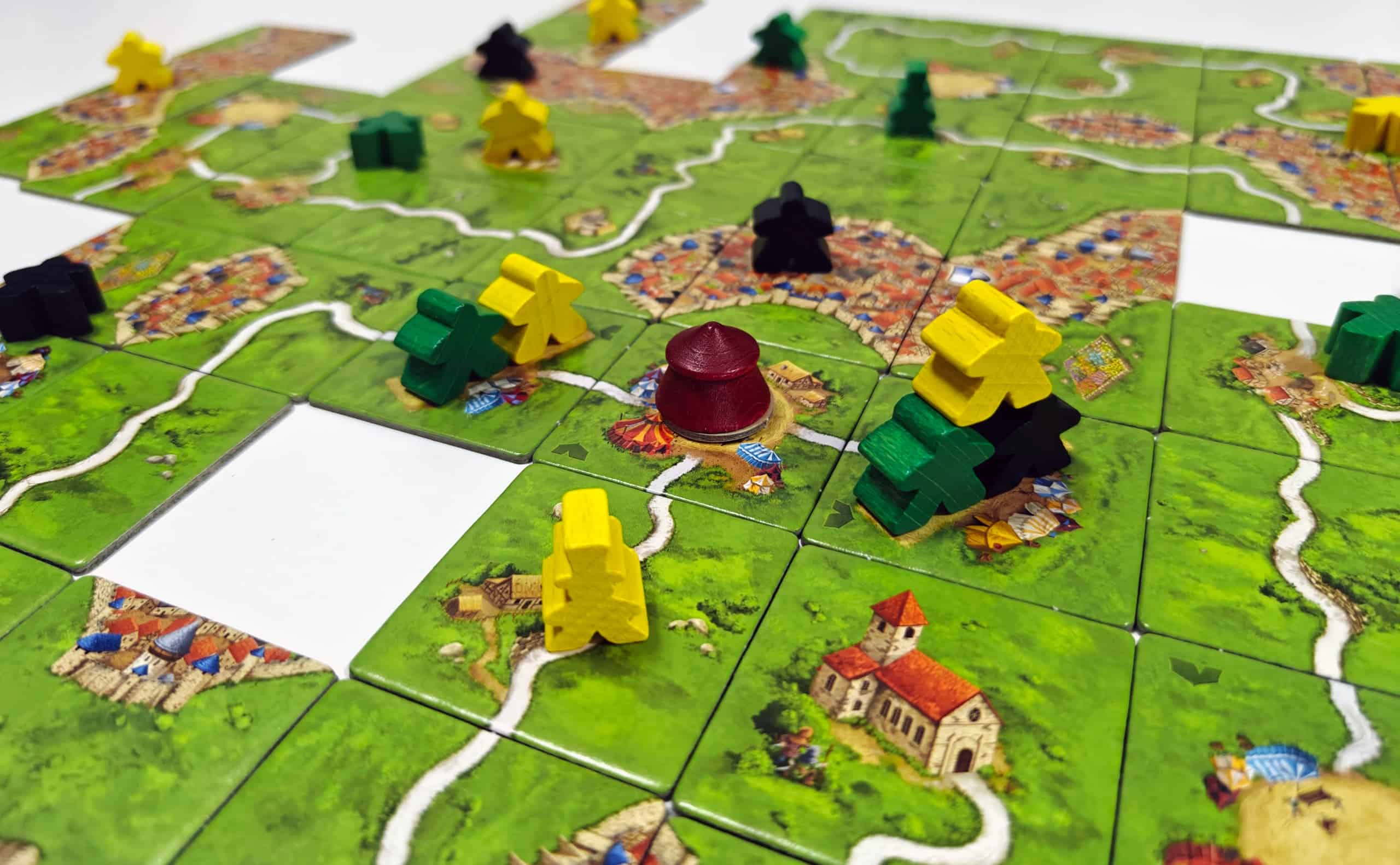 Lähikuva Carcassonne-pelialueesta. Keskellä on sirkustelttanappula, jonka alla on pistelaatta. Teltan vieressä on kaksi akrobaattipaikkaa, joista toisessa on kaksi meepleä vierekkäin ja toisessa kolmen meeplen muodostama pyramidi.