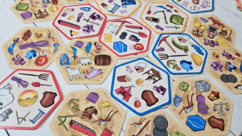 Dobble Catanin kuusikulmion muotoisia kortteja pöydällä. Korteissa on kuvattu paljon erilaisia symboleita.