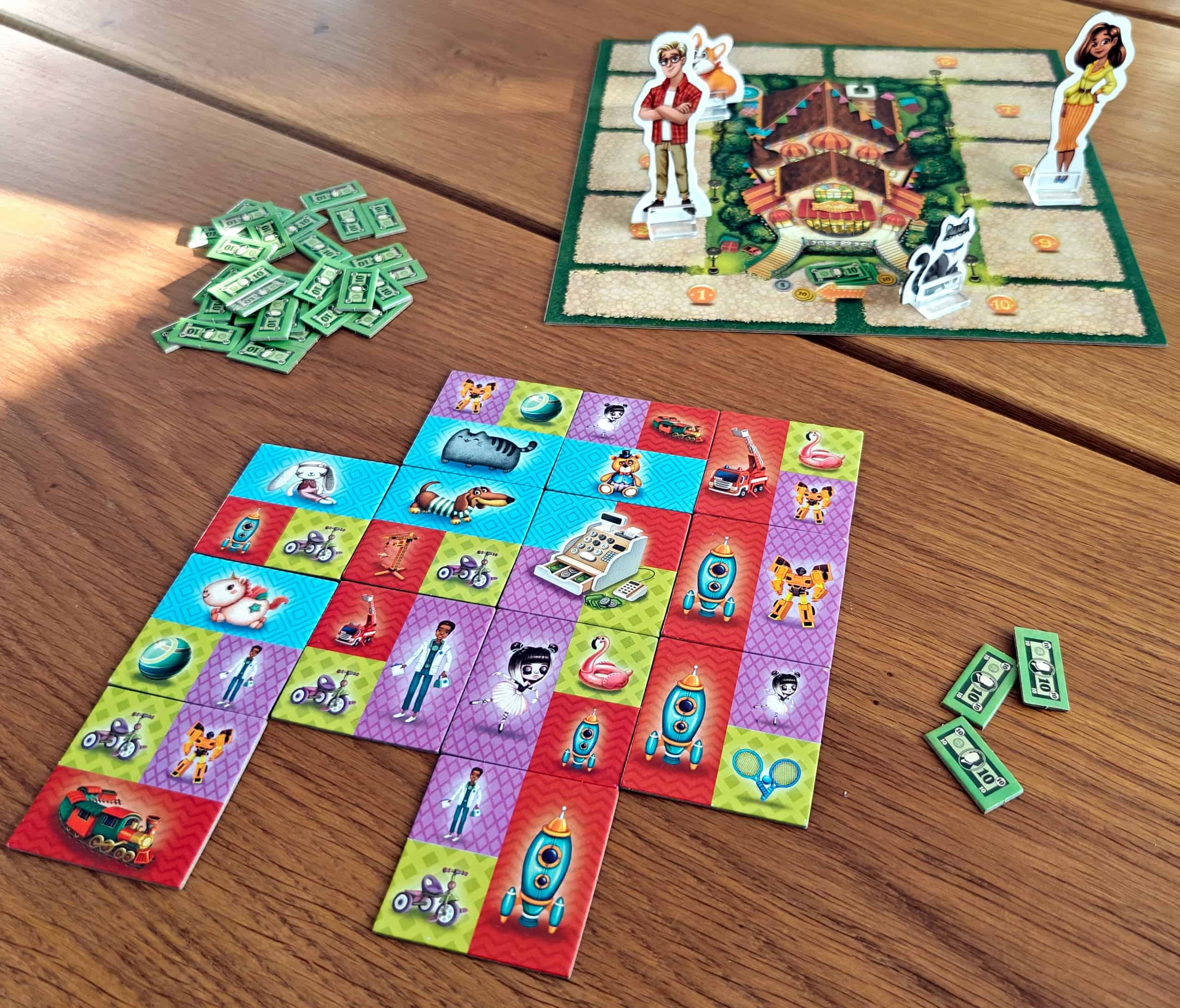 Pöydälle on rakennettu 4×4-ruudukosta kolmea ruutua vaille kaikki. Ruudukko koostuu laatoista, joissa on 2-4 eri taustaväriä ja kuvia erilaisista leluista. Taustalla näkyy lauta, jota kiertää rata. Radalla kulkee pahvihahmoja (nainen, mies, kissa ja koira).