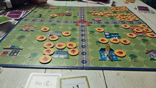 Lähikuva Pelastaja-pelin laudasta, jossa kaksi tietä muodostaa koordinaatiston. Laudalla on kuvattuna taloja, joita peittävät keltaiset liekkejä kuvaavat pahvilätkät.