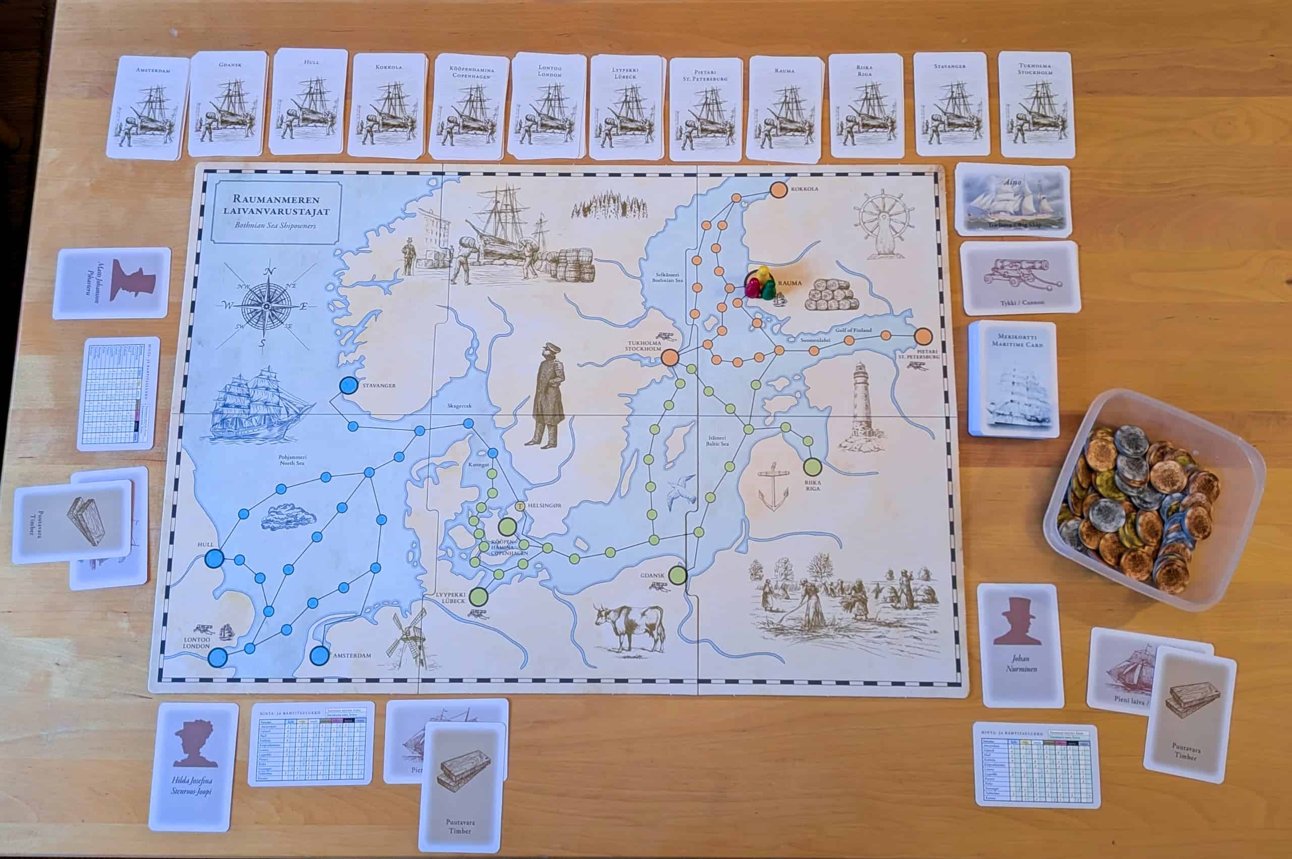 Yleiskuva Raumanmeren laivanvarustajista: pelilauta keskellä, sen ympärillä kortteja.
