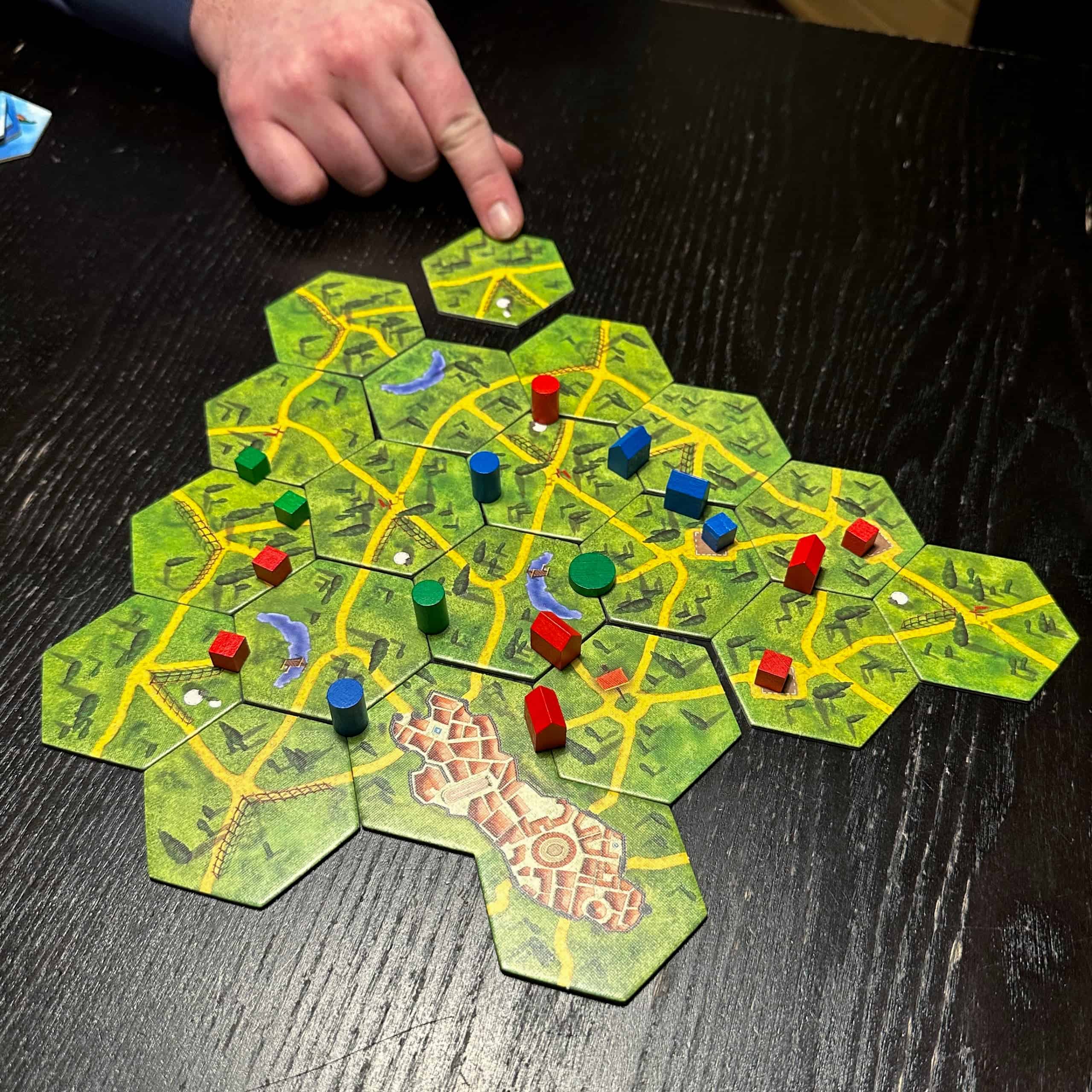 All Roadsin heksalaatoista koostuva pelialue, johon pelaajan käsi on lisäämässä yhtä laattaa. Laatoilla on keltaisia teitä vihreässä maastossa, ja tieverkosto johtaa kahden heksan kokoiselle Rooman kaupunkia kuvaavalle laatalle. Laudalla on vihreitä, sinisiä ja punaisia kuutioita, taloja, kiekkoja ja sylintereitä.