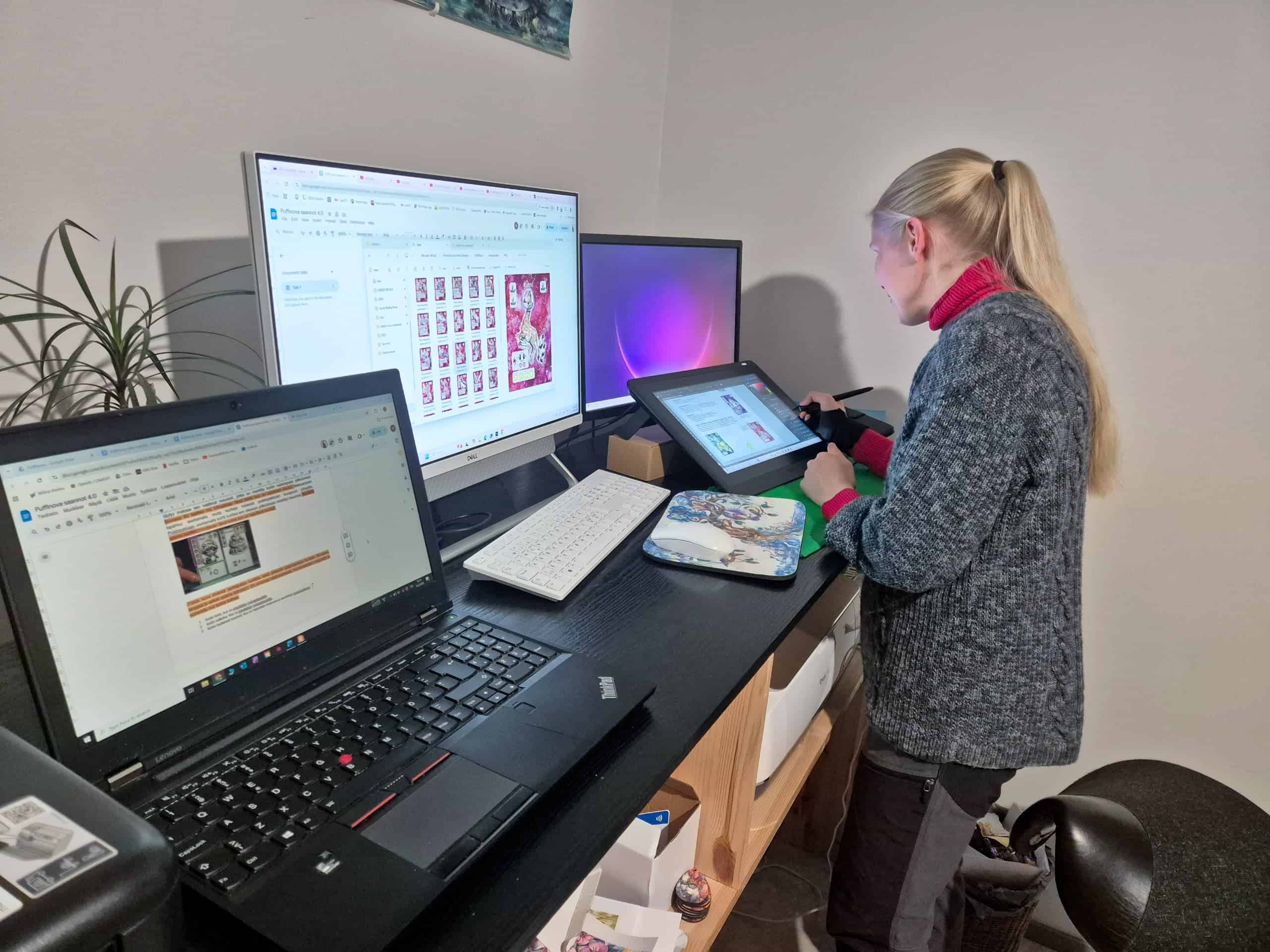 Jasu Hintsala työskentelemässä piirtopöydällä. Pöydällä on kaksi isoa näyttöä, näppäimistö ja avoin läppäri. Isolla näytöllä ja läppärillä on avoinna PuffiNovan materiaaleja.