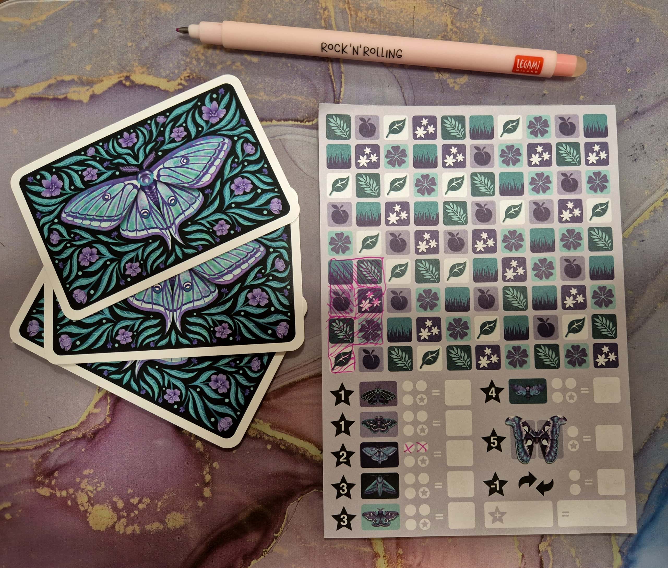 Nocturnis-pelin kuponki, jossa on 10×9-ruudukko erilaisia kasvisymboleita. Kupongin vieressä on kolme korttia, joissa on yöperhosen kuva.