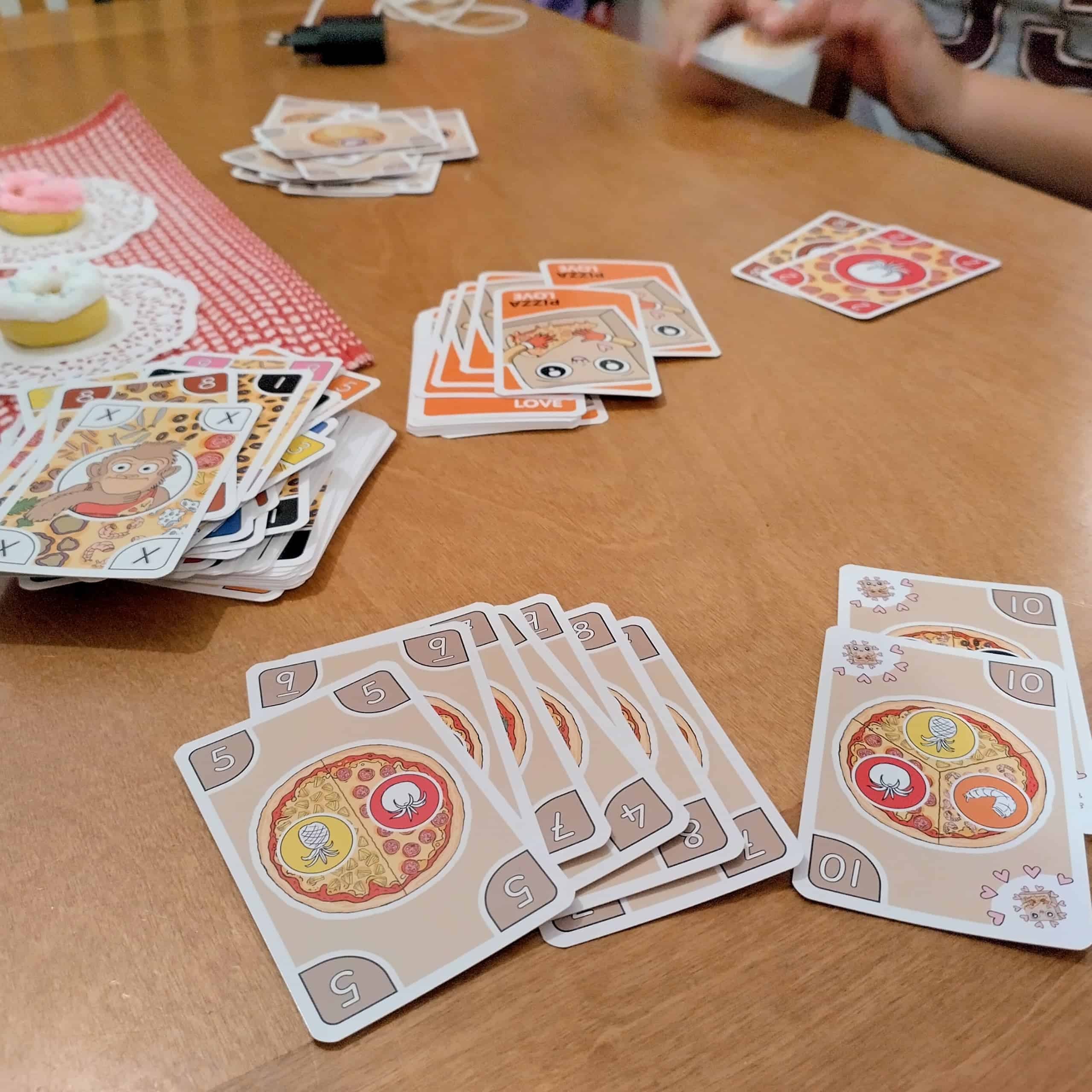 Pitsakortteja pöydällä, taustall apino käytettyjä täytekortteja ja nostopakka.