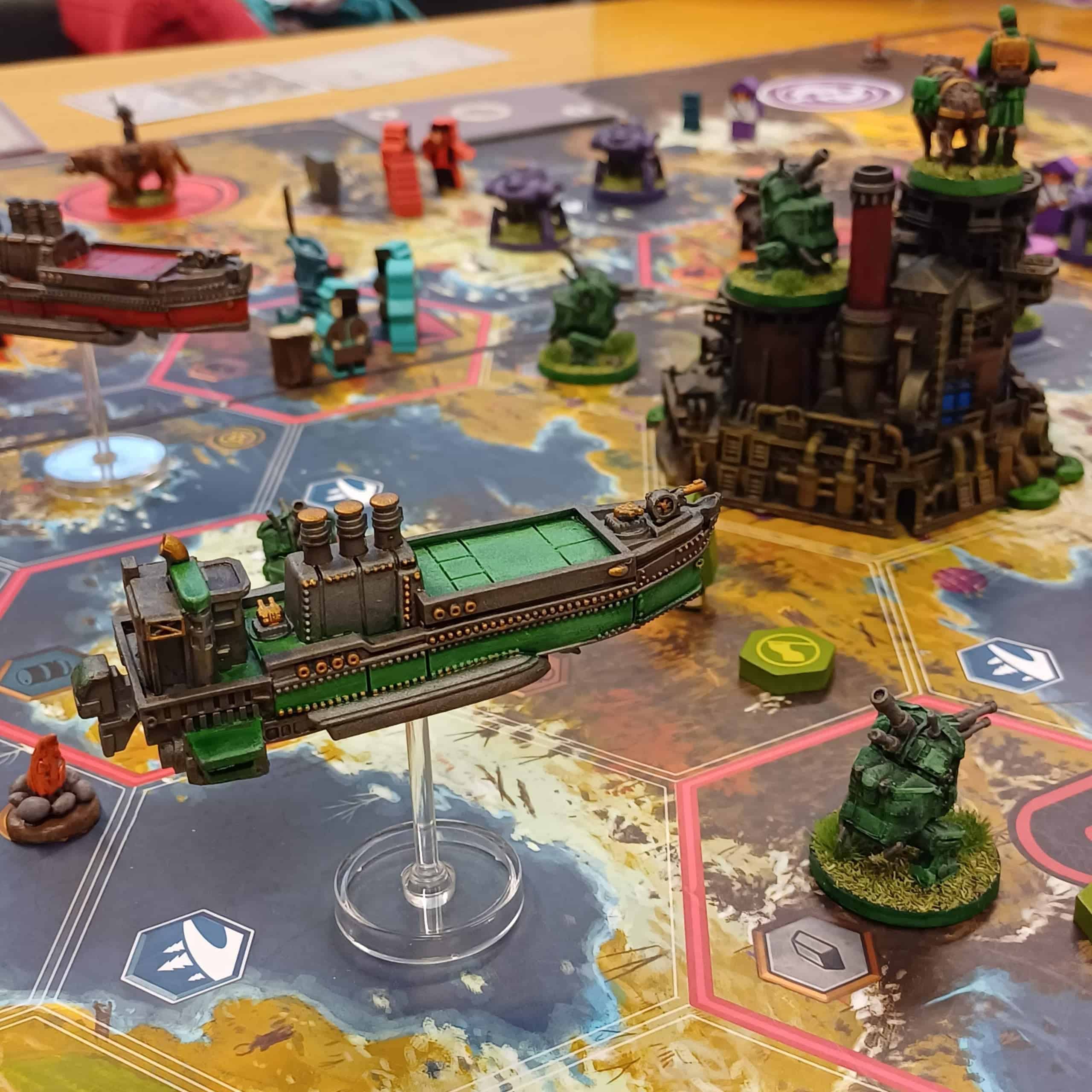 Lähikuva Scythen pelilaudasta, jossa on hienoja maalattuja ja kustomoituja komponentteja. Etualalla on valtava muovijalustan varassa lentävä steampunk-lentolaiva.