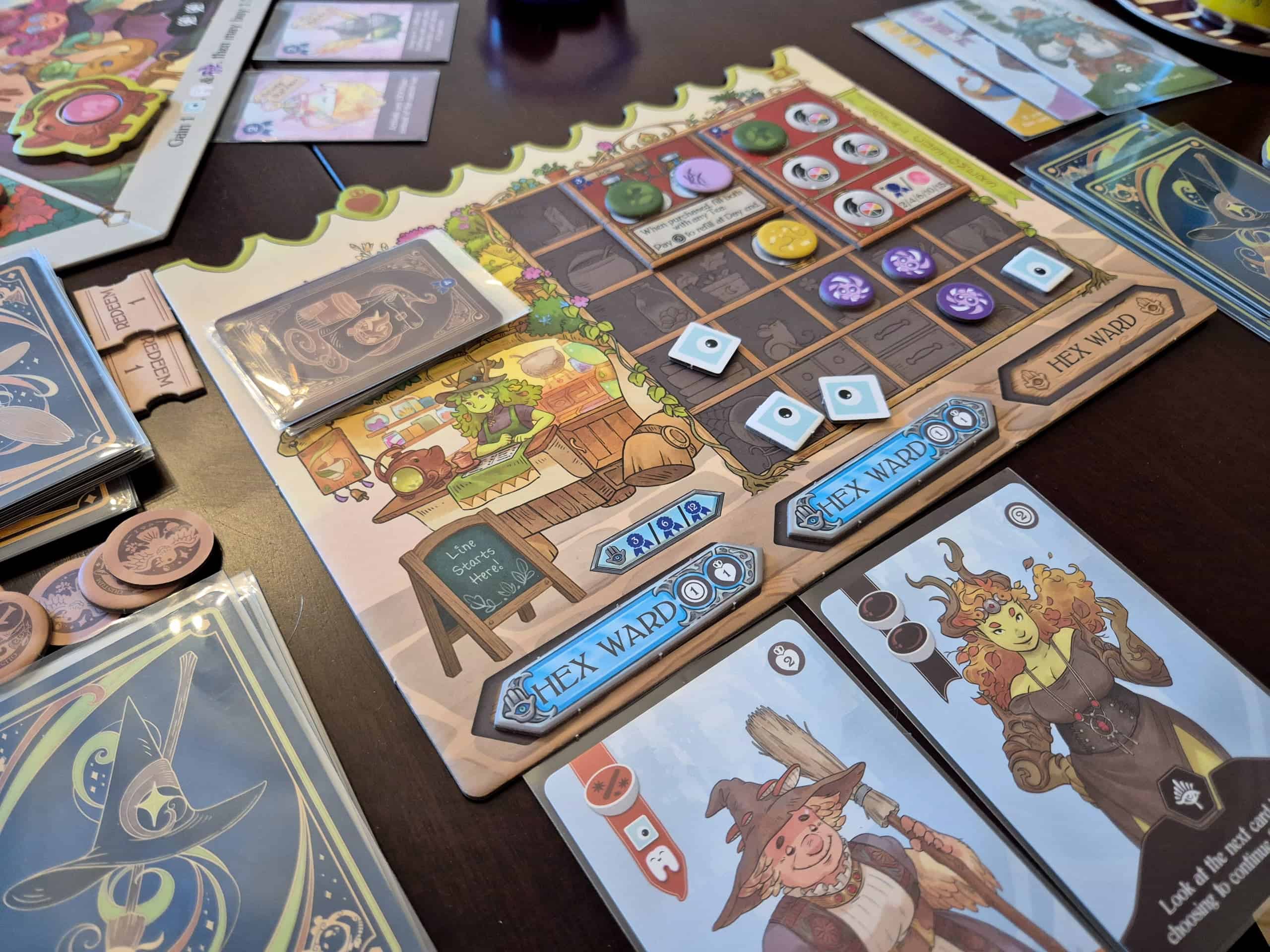 Lähikuva Tea Witchesin pelilaudasta ja korteista. Laudalla on kuvattuna vihreän satuolennon pitämä teekauppa, joka on pelissä 5×5-ruudukko.