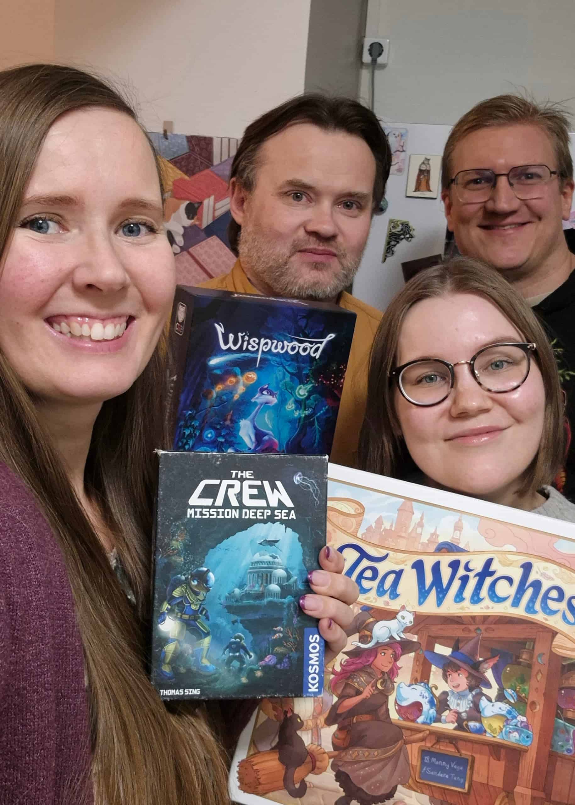 Valokuvassa neljä henkilöä, joilla käsissään lautapelejä: Tea Witches, The Crew: Mission Deep Sea ja Wispwood.