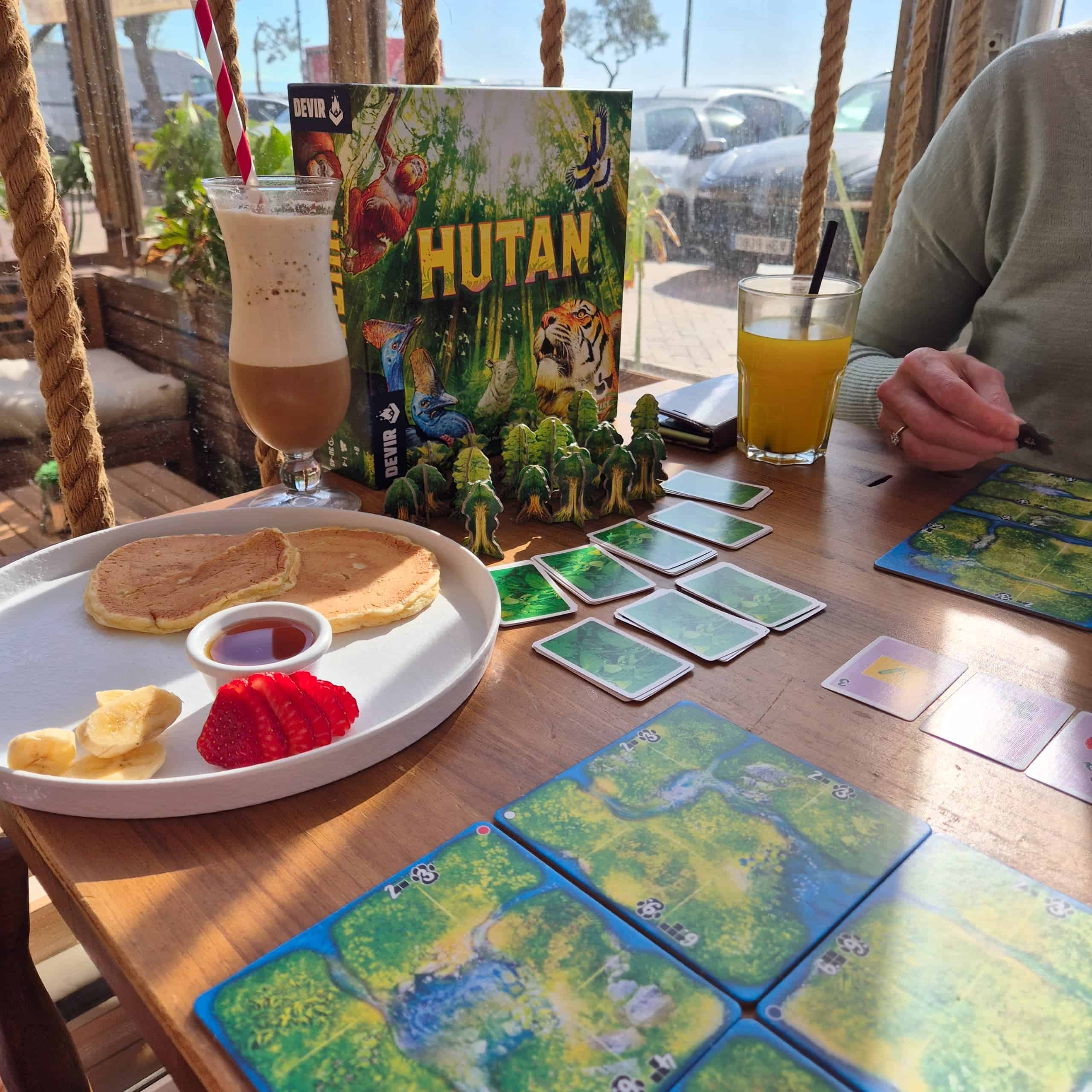 Hutan-peli pöydällä Fuengirolan Riviera Maya -kahvilassa. Pöydällä pannariannos ja juomalaseja ja pelin laatikko pystyssä.