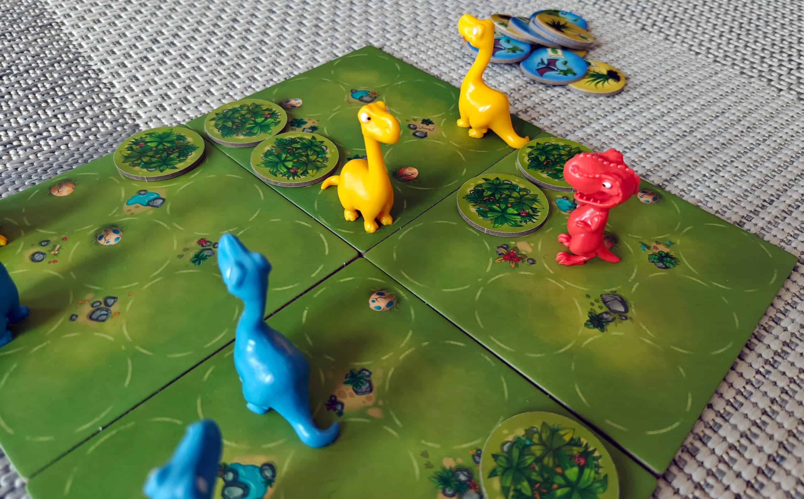 Jurassic Snackin pelilauta, jossa on punainen muovinen Tyrannosaurus Rex ja kaksi keltaista ja kolme sinistä Diplodocusta.