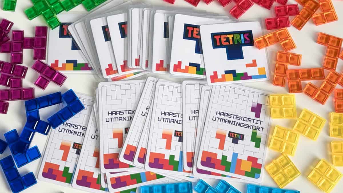 Tetris-pelin kortteja, ympärillä eri värisiä muovisia läpikuultavia tetromino-palasia.