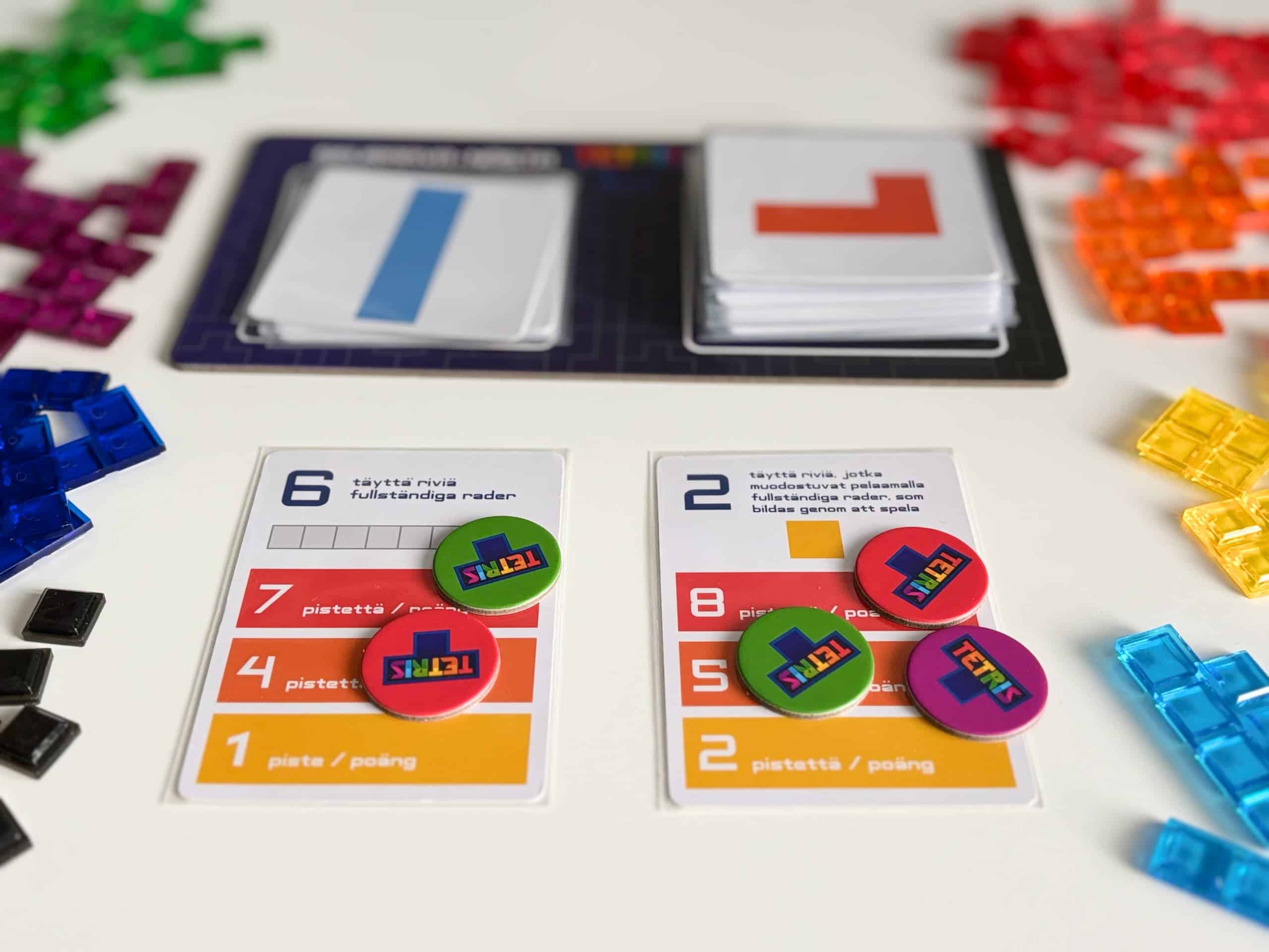 Kaksi tavoitekorttia, "kuusi täyttä riviä" ja "kaksi täyttä riviä, jotka muodostuvat pelaamalla neliön". Taustalla näkyy nykyinen pala (neljän suora) ja seuraava pala (L-mutka).