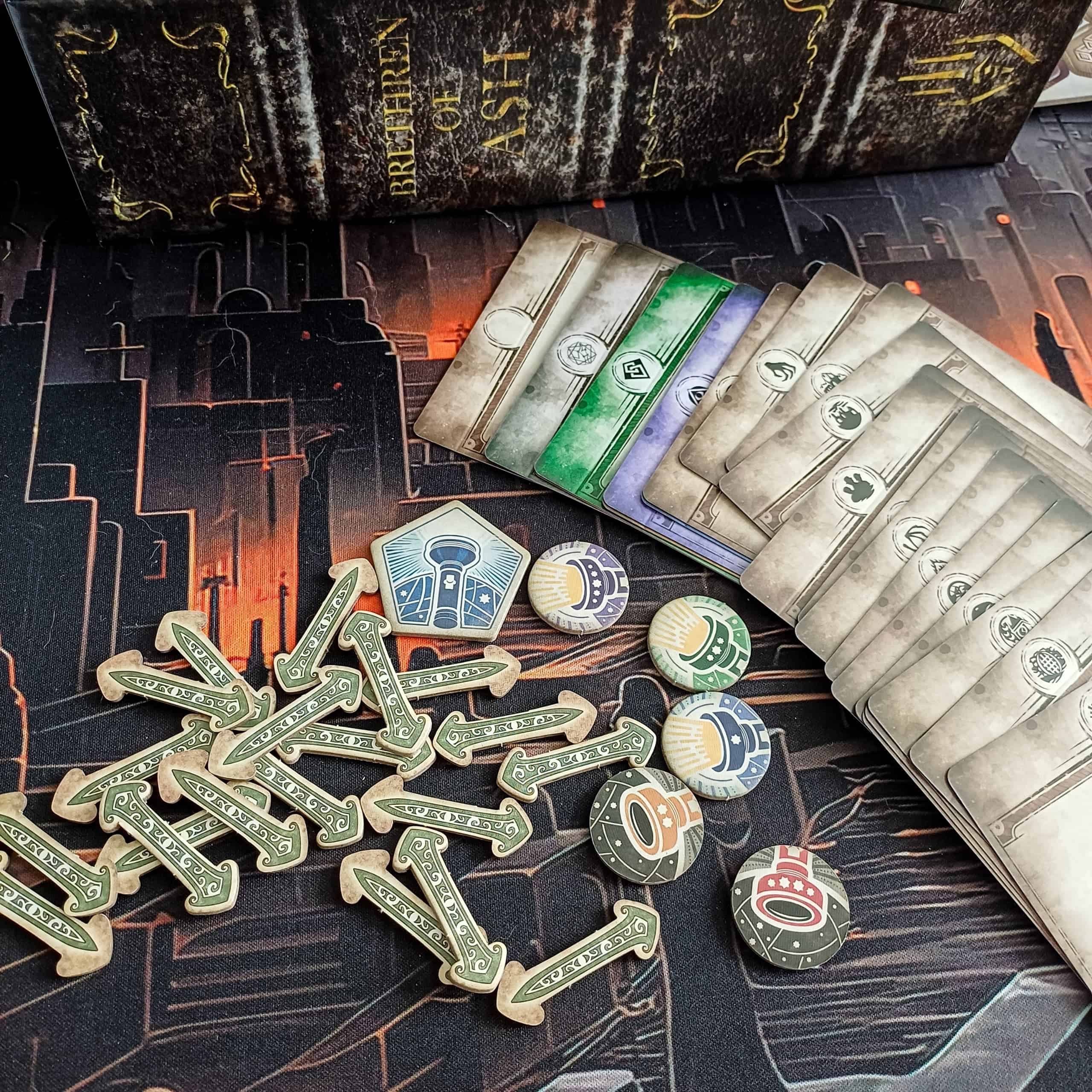 Valikoima Arkham Horror Card Gamen komponentteja, kuten pahvisia nuolia ja tokeneita ja erilaisia korttisetin välikortteja.