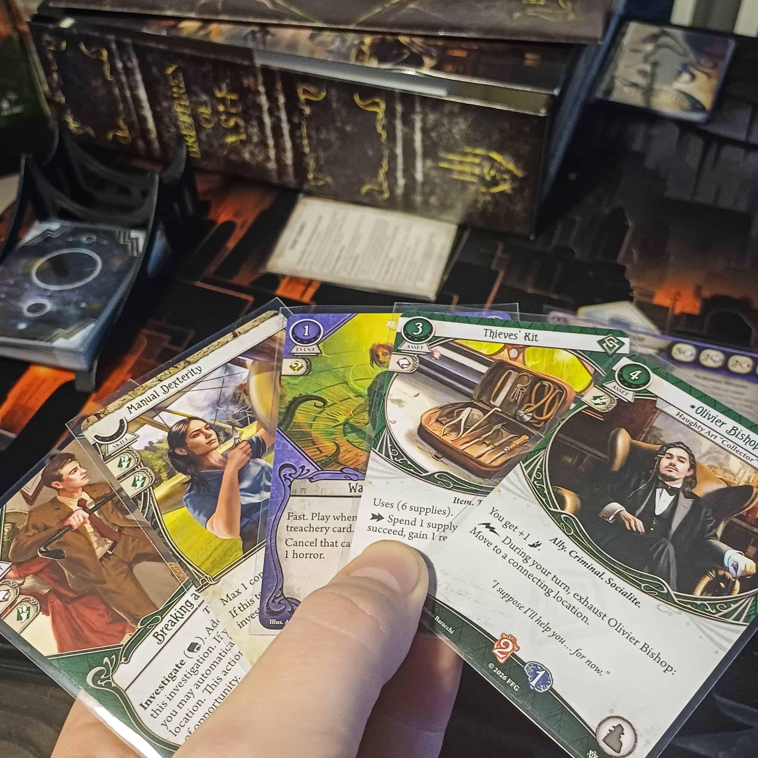 Käsi, joka pitelee viuhkassa viittä korttia. Korteista erottuvat Manual Dexterity, Thieves' Kit ja Olivier Bishop.