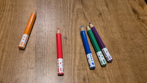 Pick a Pen: Gardensin kyniä pöydällä. Viisi eri väristä kynää, kaikissa tyvessä noppakuviointi.