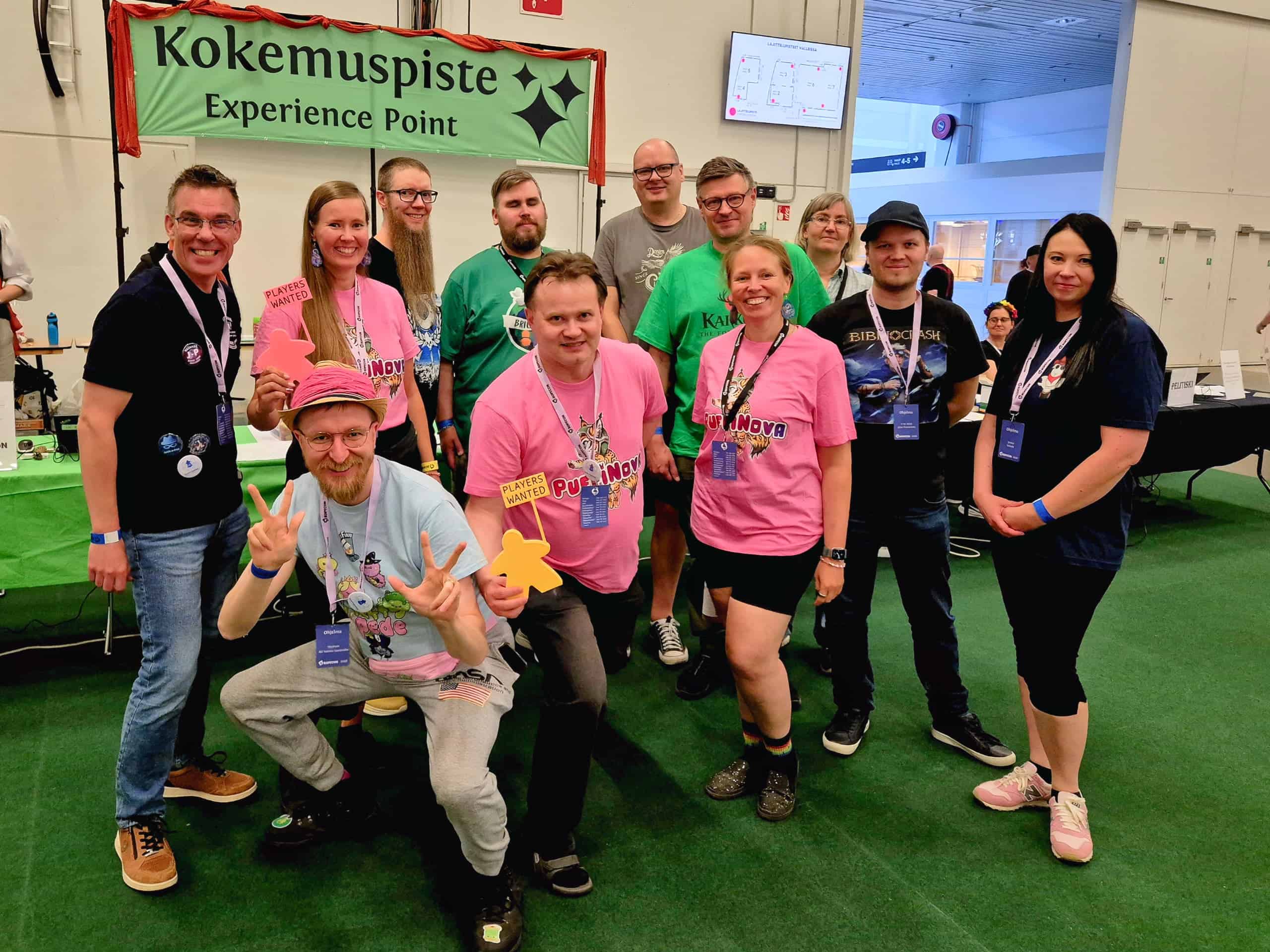 Kahdentoista henkilön ryhmäkuva Ropeconissa Kokemuspisteen edustalla.