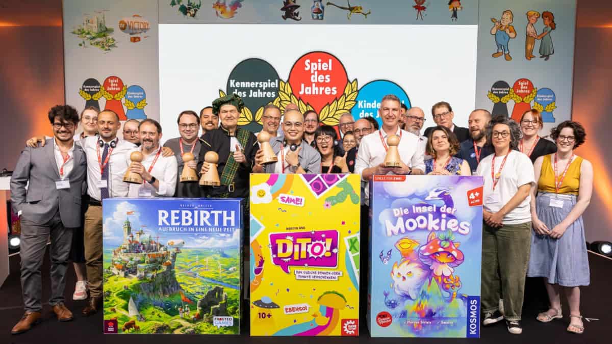 Spiel des Jahres -voittajat. Etualalla kolmen voittajapelin (Rebirth, JinxO, Mooki Island) jättikokoiset kannet ja niiden takana 27 ihmistä eli voittajapelien tuotantotiimit. Laatikoiden takana on pelien suunnittelijat Reiner Knizia, Martin Ang ja Florian Sirieix.