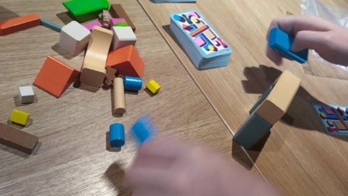 Rakenna ja arvaa -pelin palikoita pöydällä ja pelaajan sumeat kädet, jotka ovat rakentamassa palikoista jotain.